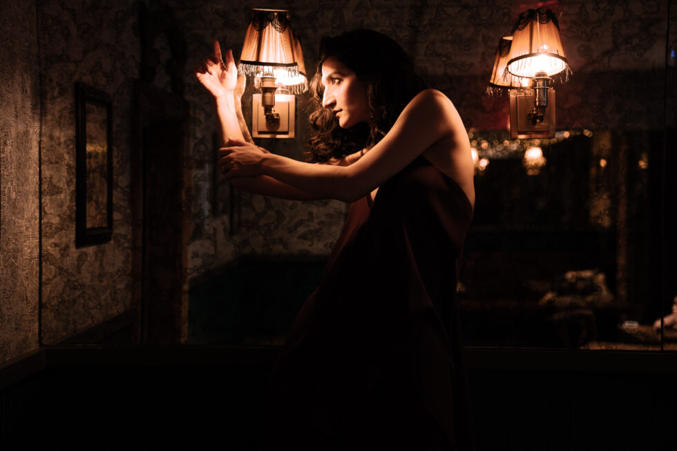 A female dancer moving next to vintage lamps in a dimly lit room.
