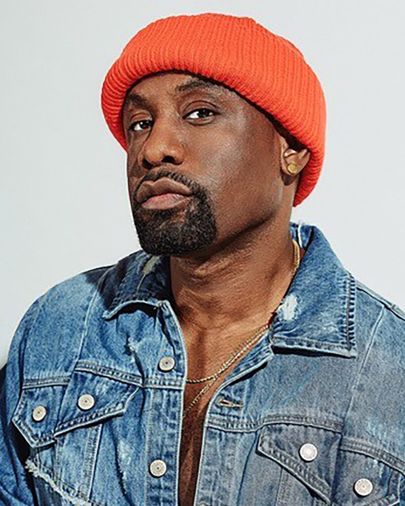 Draico Johnson, wearing a bright orange beanie and a light denim jacket, tilts his chin up slightly as he looks into the camera lens for a headshot.