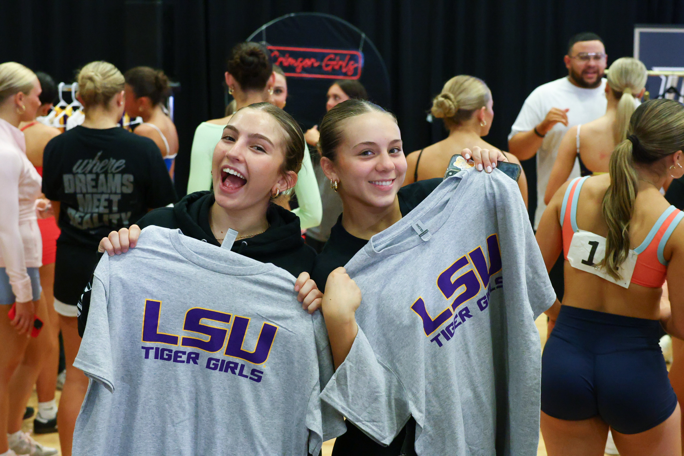 Two dancers smile and hold up gray t-shirts with the Louisiana State University Tiger Girls logo on them.
