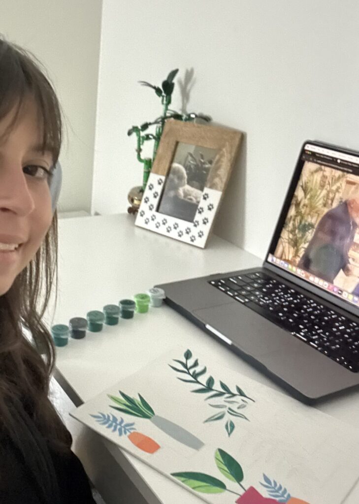 Katie Tapalaga poses by her desk, which houses a laptop and a paint-by-numbers project.