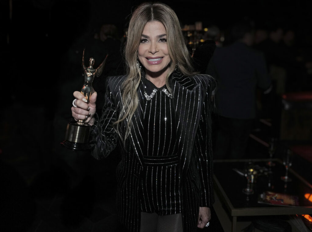 Paula Abdul, in a black dress with a collar, smiles while holding out her World Choreography Award.